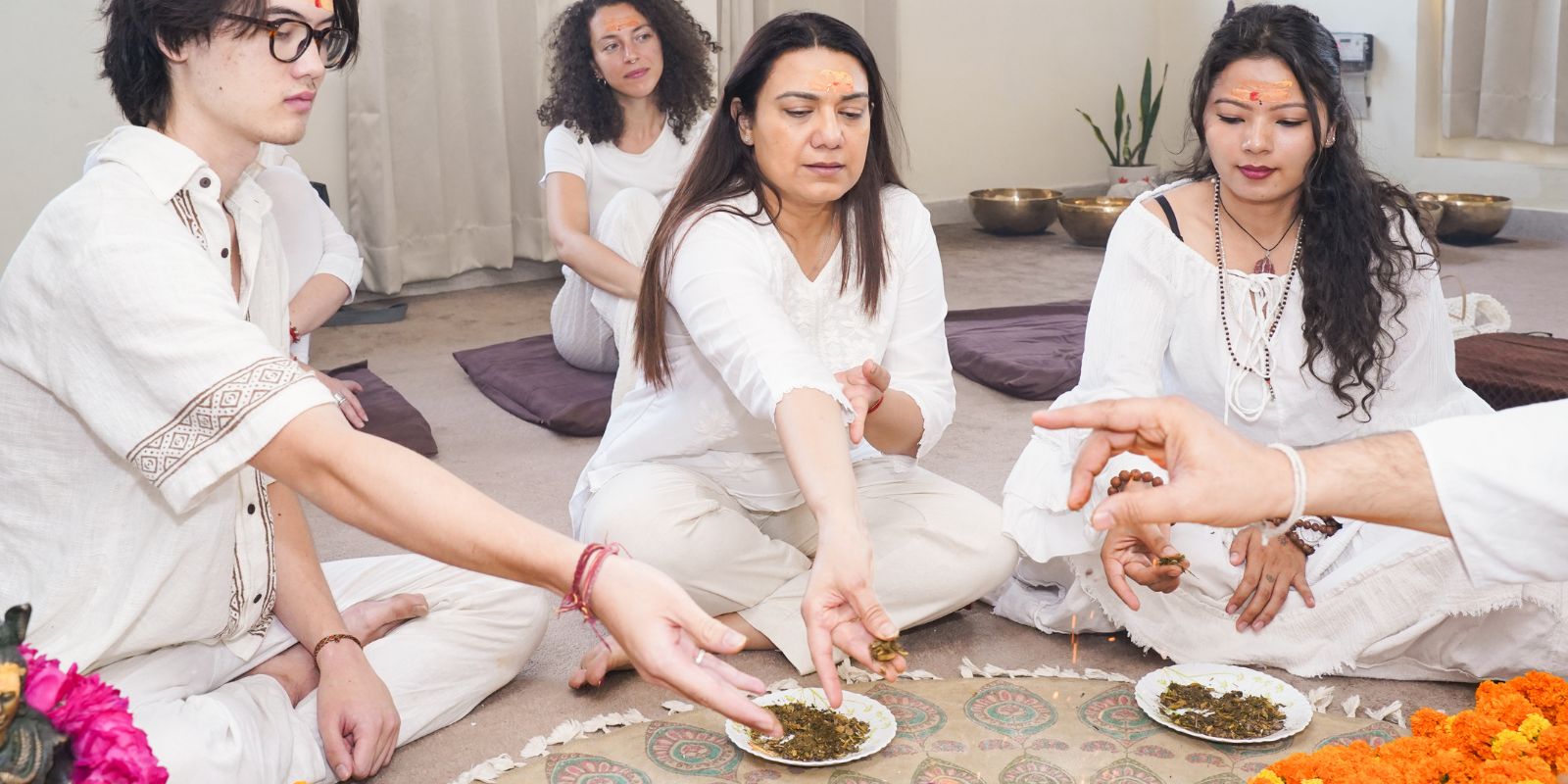 Participants dressed in white during a traditional healing ceremony, respectfully offering herbs or sacred materials into ritual plates as part of a spiritual practice at Yogshri Healing Center.