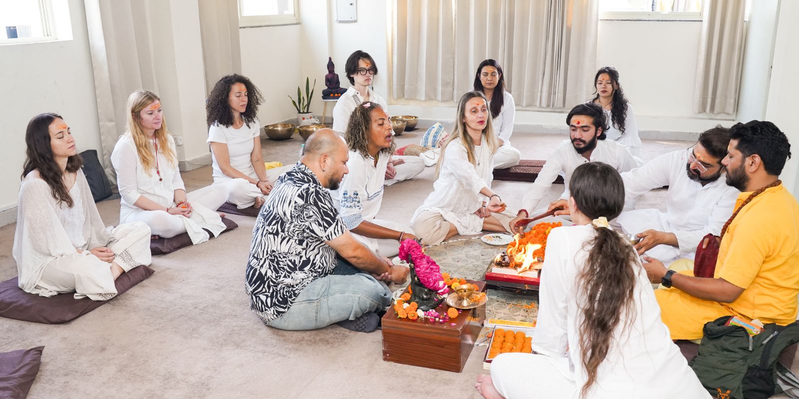 Group of individuals participating in a sacred fire ritual (Havan) at a wellness retreat, seated in a circle wearing white attire, engaging in spiritual chanting and meditation.