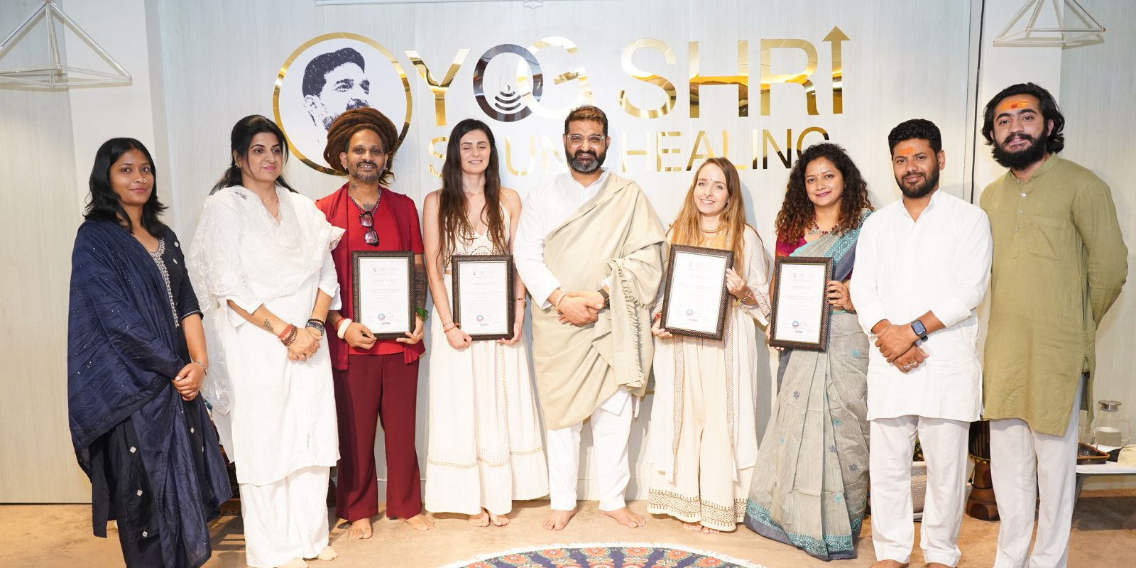 Group photo of Yogshri Healing Center team and students proudly holding certificates after completing a spiritual or healing training program, standing in front of the Yogshri logo wall.