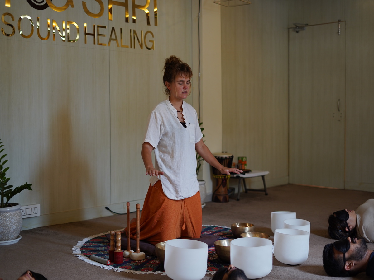 A sound healer leading a session with crystal singing bowls and Tibetan bowls at Yogshri Sound Healing, while participants lie down in meditation.